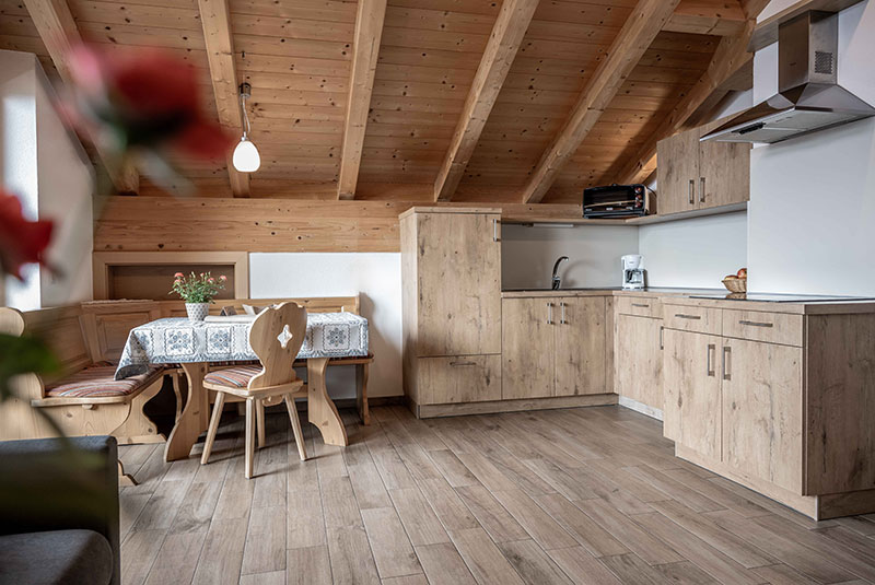 Wohn- und Essbereich mit Sofa, Eckbank und Tisch, auf der linken Seite eine hölzerne Kochnische - Oberhof Weitental